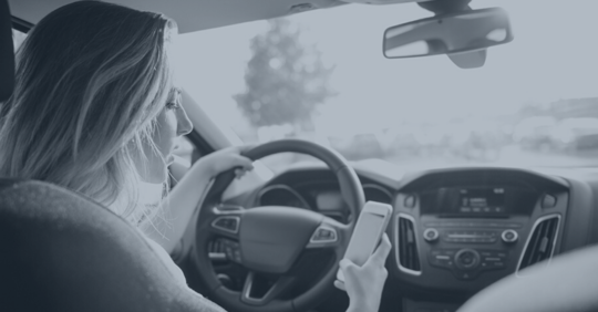 Woman driving and looking at her cell phone.