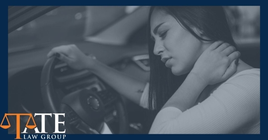 Woman in drivers seat of her car holding her hand on her neck as if she's in pain.